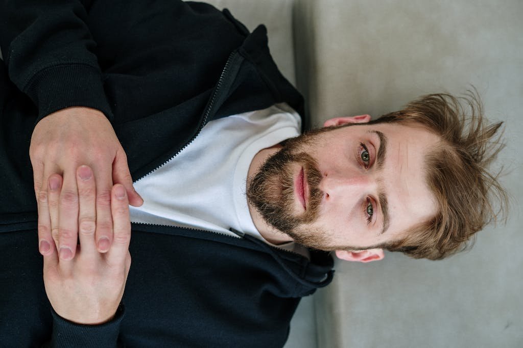 A thoughtful bearded man lying down, appearing contemplative, captured indoors.