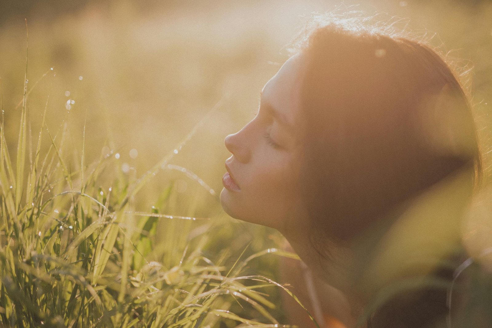 Serene portrait of a woman in a sunlit grassfield, eyes closed, embracing tranquility.