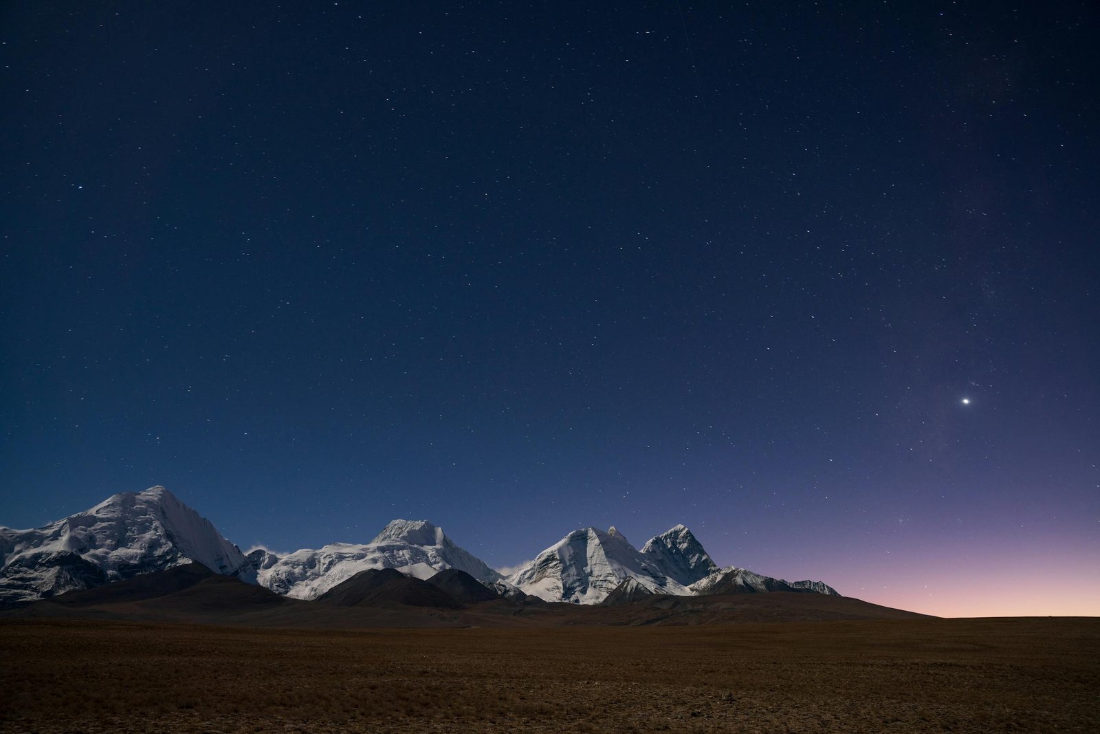 A breathtaking view of snow-capped mountains under a starlit sky at twilight.