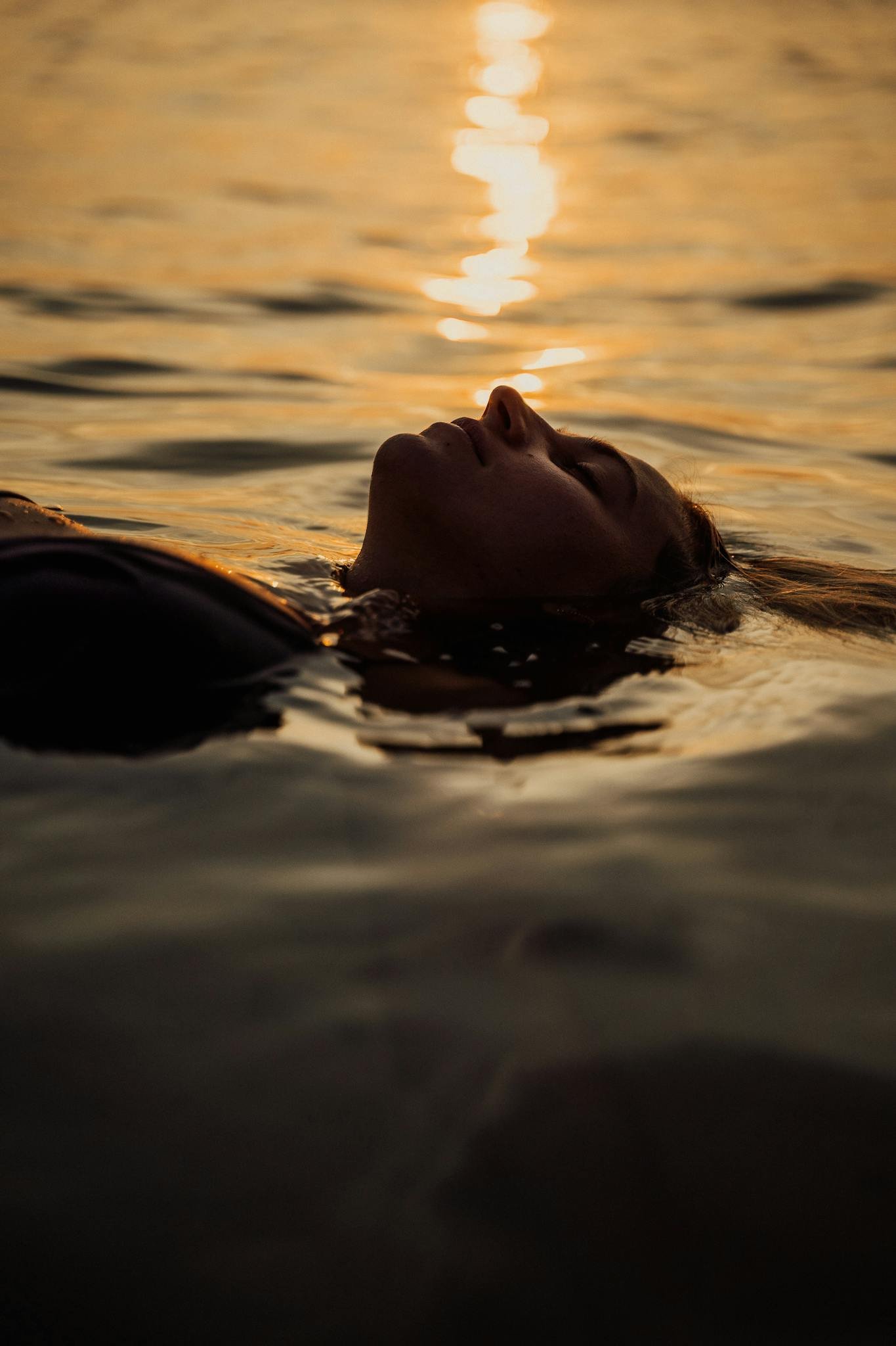 A woman floats peacefully in the ocean at sunset, capturing serenity.