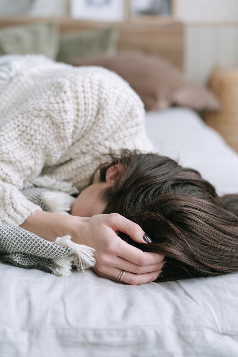 A woman in a knitted sweater peacefully resting on a bed, capturing a serene indoor moment.