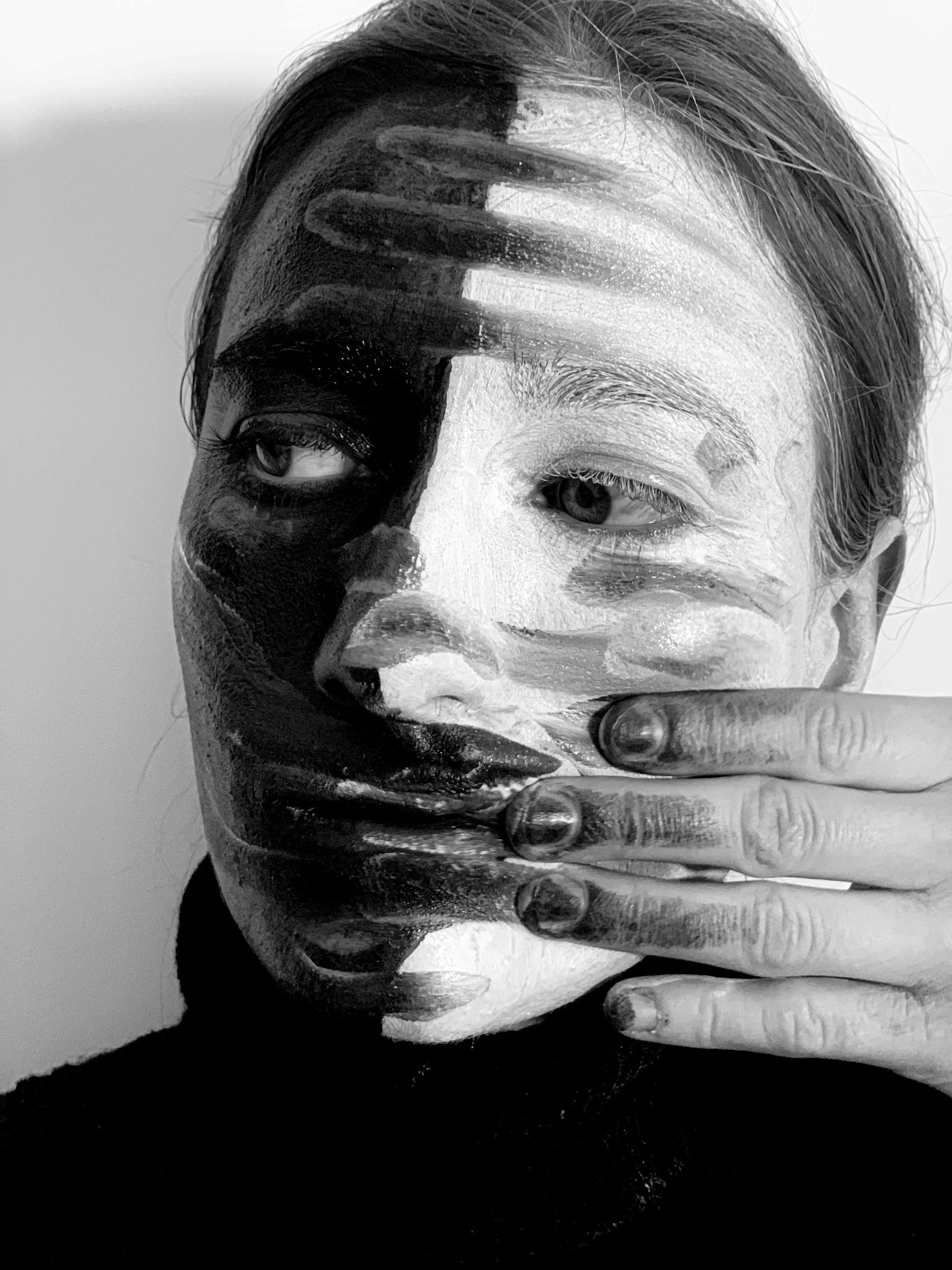 Black and white headshot of strange female smearing paints on face with dirty hand and looking away while standing on white background