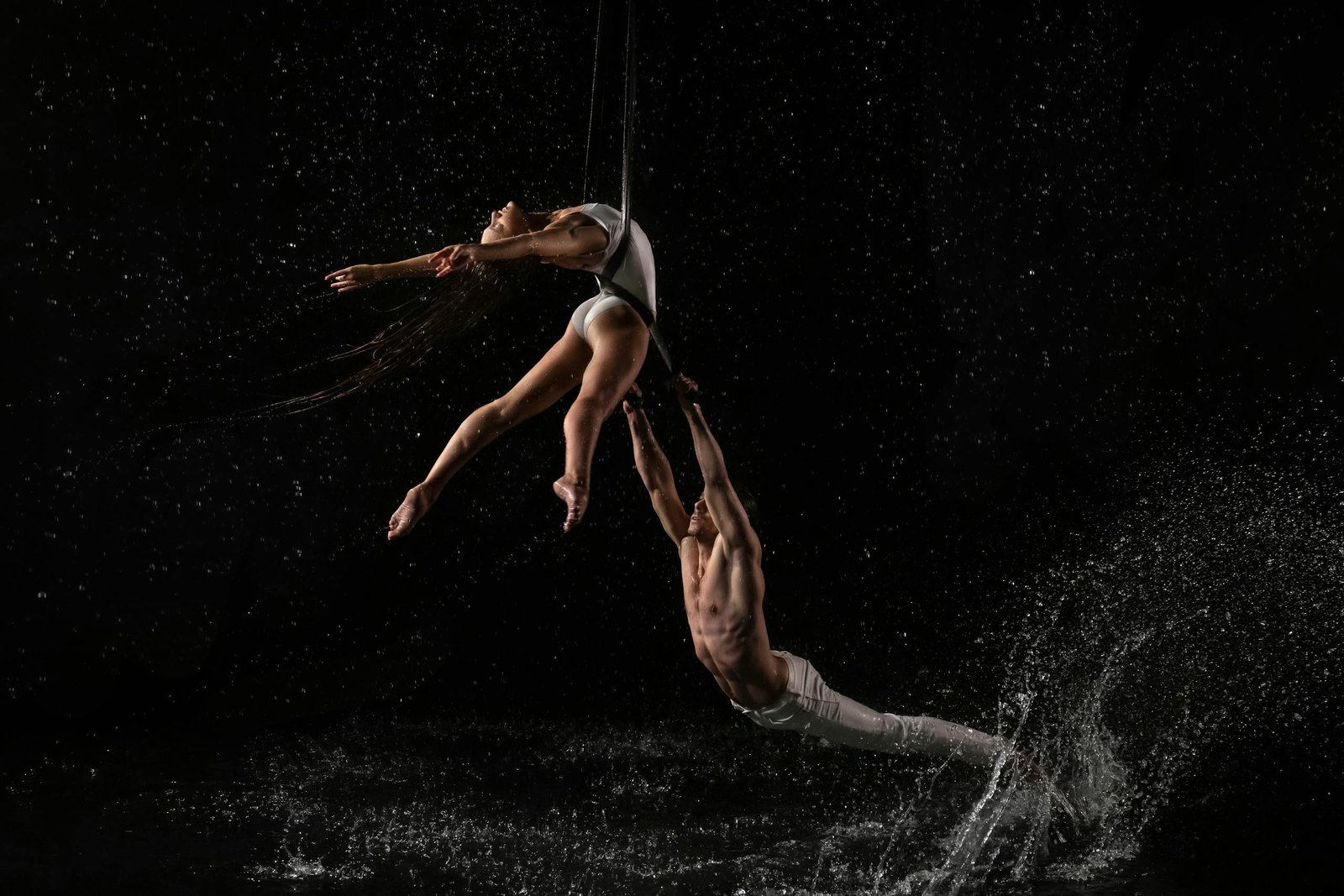 Captivating aerial dance with dynamic water splashes against a dark background.