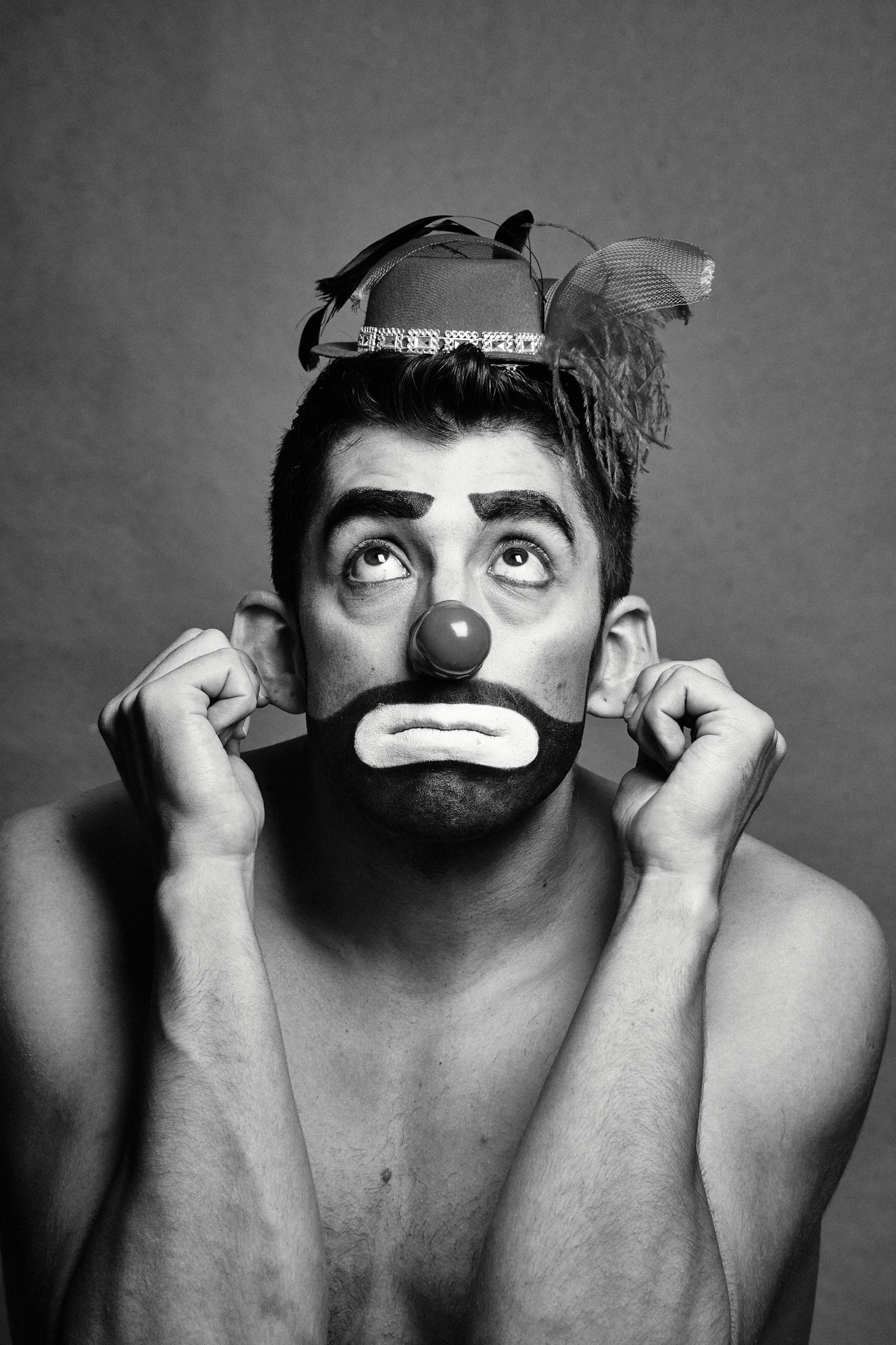 Dramatic black and white portrait capturing a sad clown looking upward, wearing a classic hat.