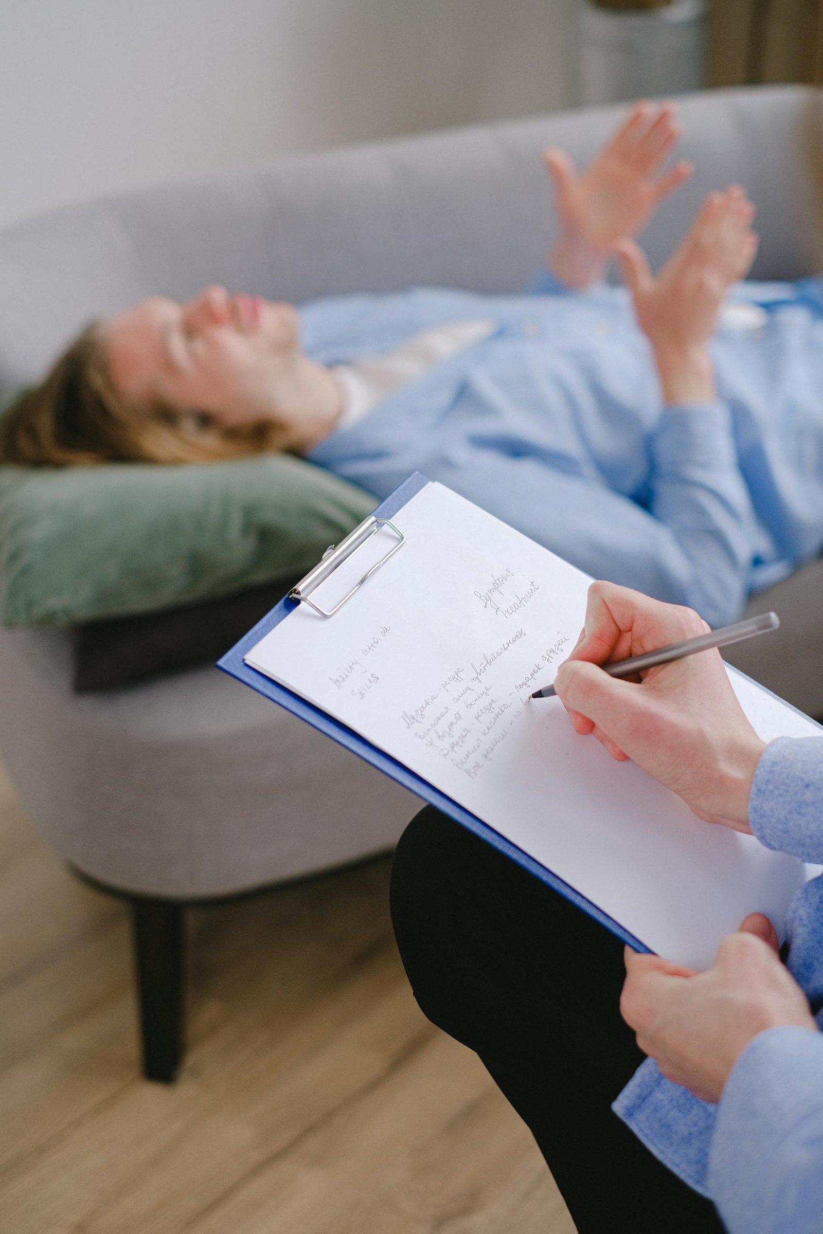 Therapist taking notes while a patient lies on the couch during a therapy session.