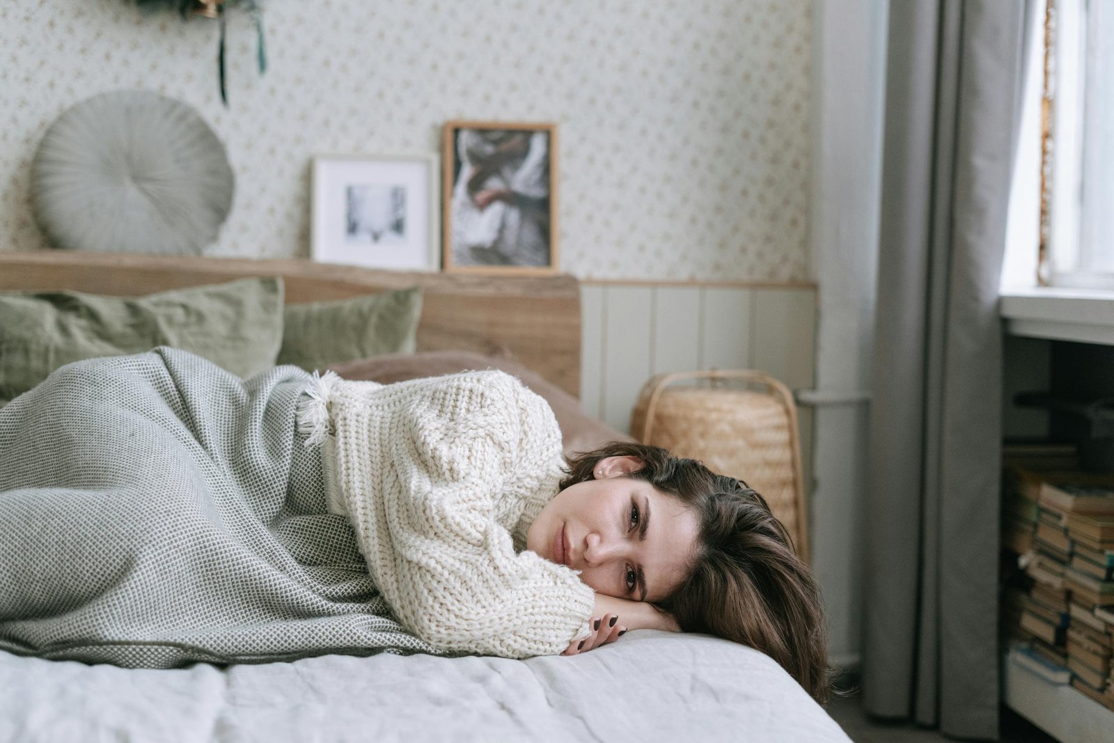 A woman in a knitted sweater lies on a bed, creating a cozy atmosphere.
