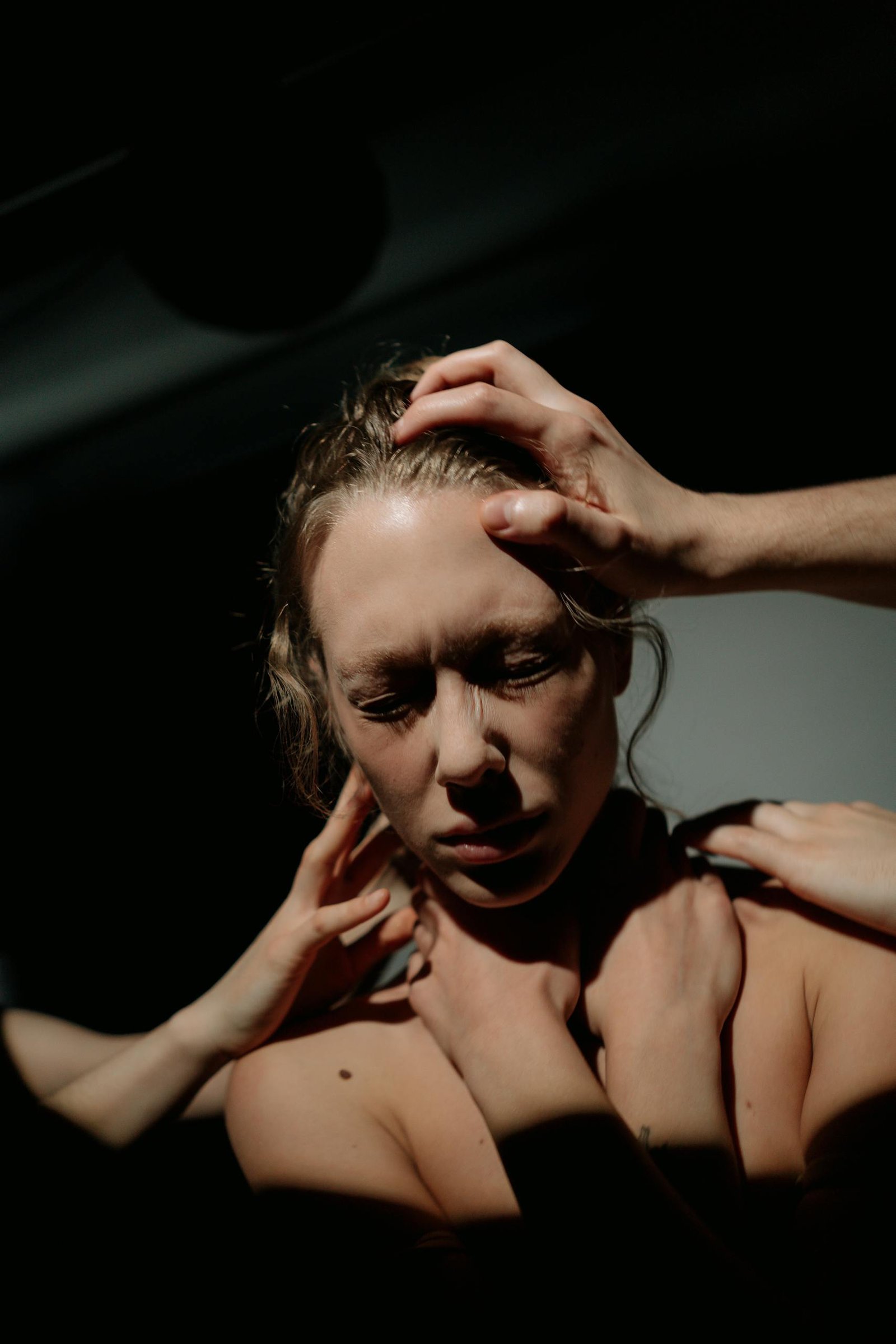 Dramatic lighting on a woman expressing deep emotional distress, surrounded by hands.