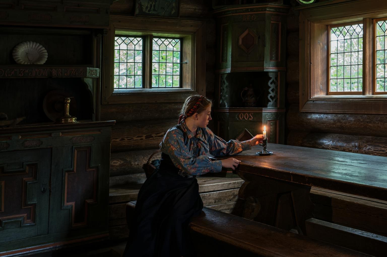 A woman sits by candlelight in a vintage wooden room, exuding a warm and nostalgic ambiance.